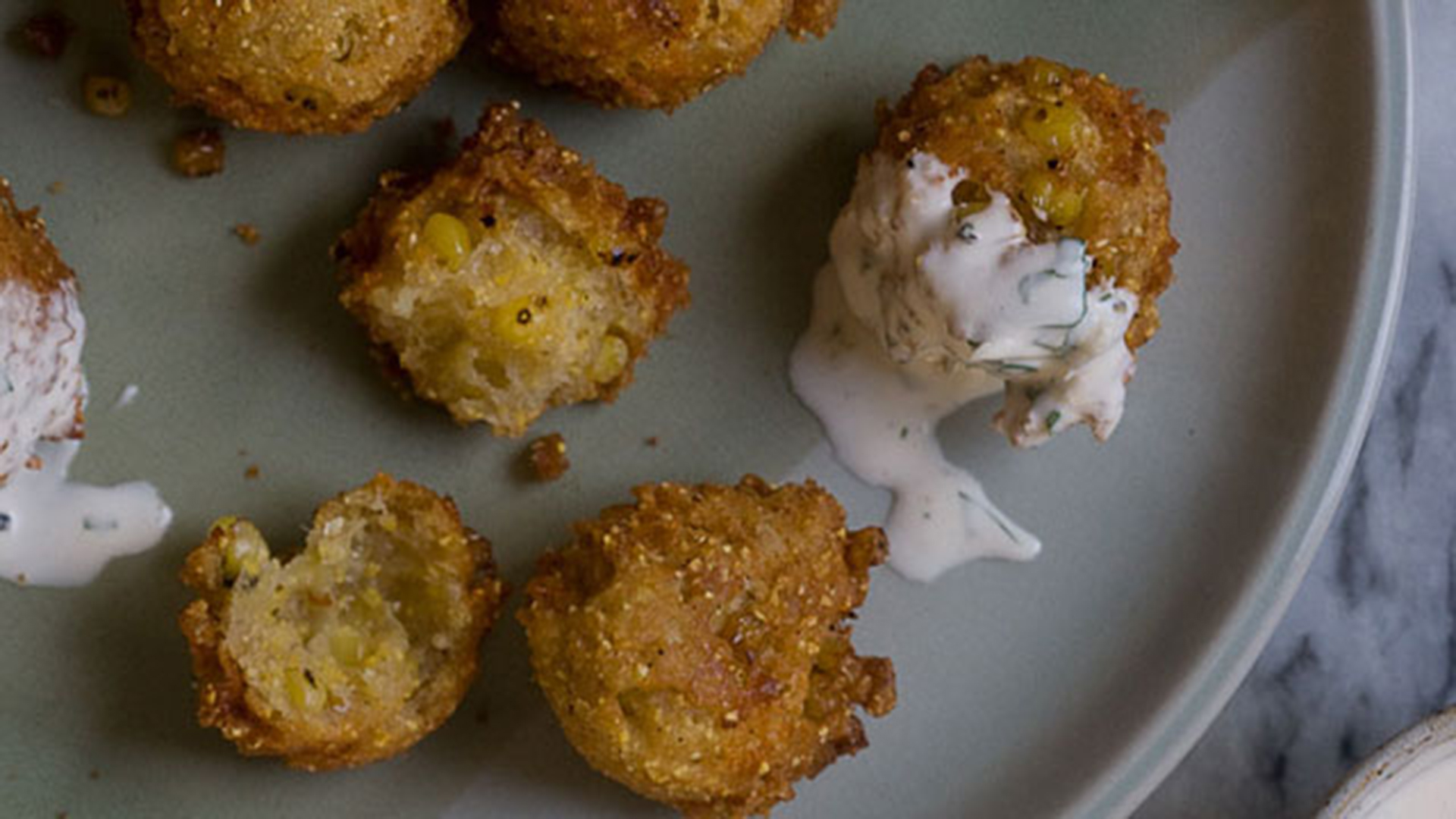 Charred corn fritters on a plate drizzled in ranch dressing.