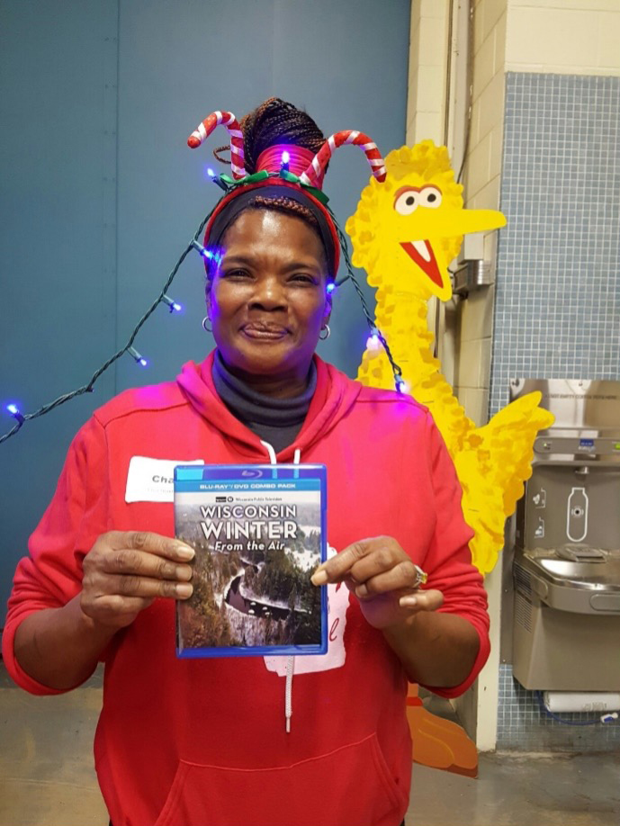 Braxton with Big Bird in the background and candy canes in her hair, holding up a DVD copy of "Wisconsin Winter from the Air"