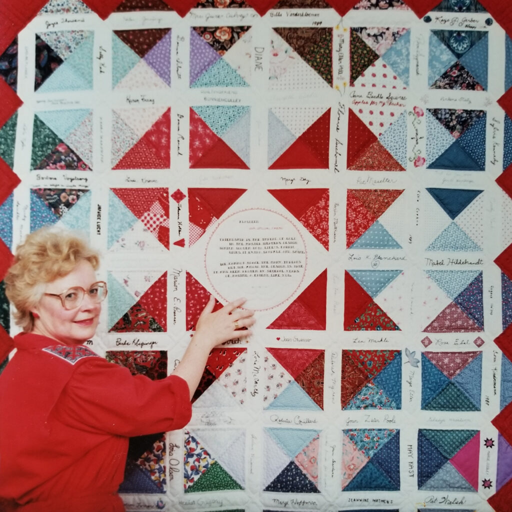 Klaudeen stands in a red dress next to her 50th birthday quilt.