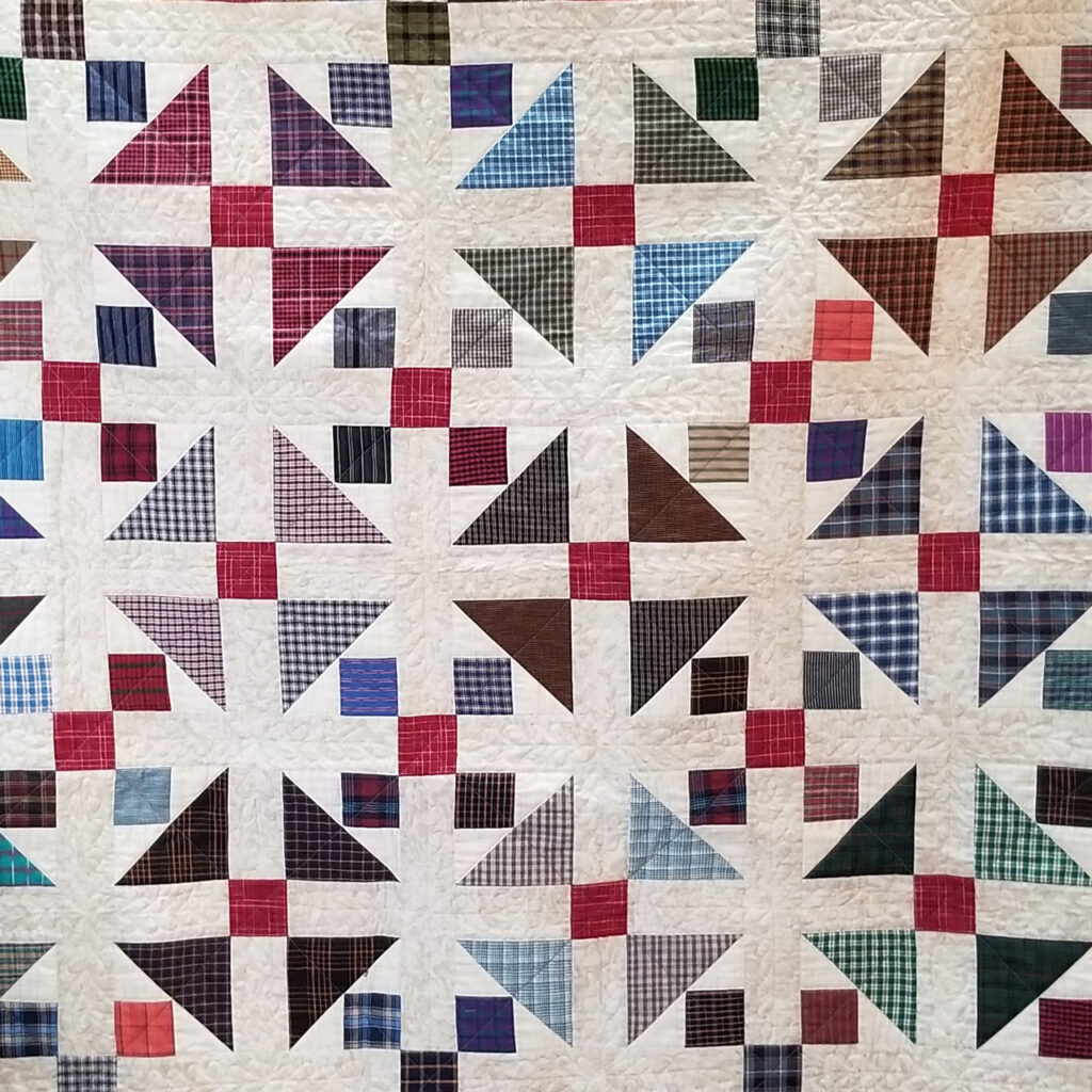 A traditional quilt with a white background and a grid of triangles in mostly cool colors broken up with a pattern of small red squares. 