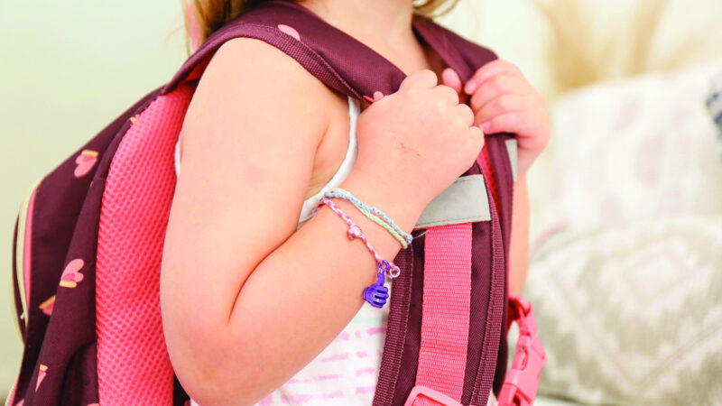 Close-up of a young child wearing a backpack and a homemade bracelet.