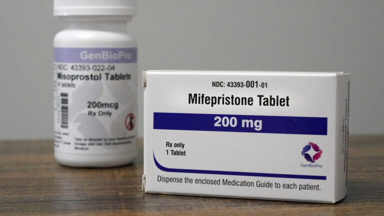A cardboard medication box with the labels Mifepristone Tablet and 200 mg sits on a table in front of a plastic medication bottle with the same labels.