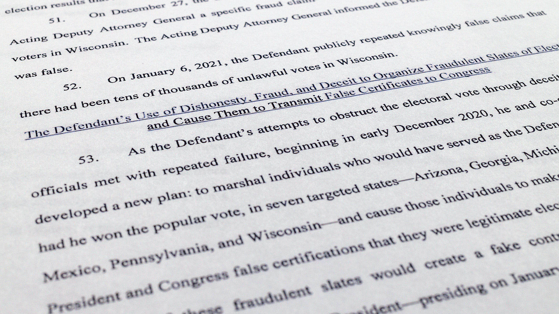 Printed text on a piece of paper reads "The Defendant's Use of Dishonesty, Fraud and Deceit to Organize Fraudulent Slates of Electors and Cause Them to Transmit False Certificates to Congress" with additional text above and below describing a count in an indictment.