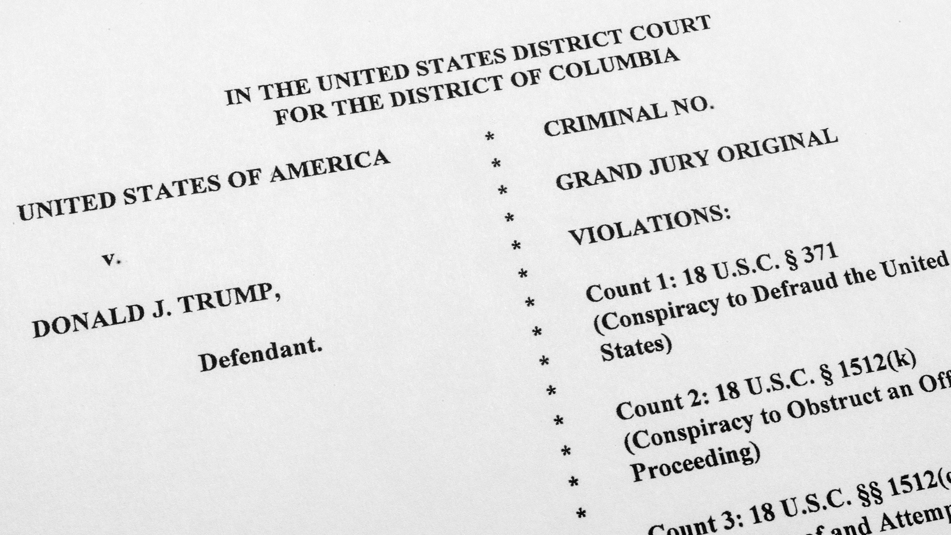 Printed text on a piece of paper reads "In the United States District Court for the District of Columbia" and "United States of America v. Donald J. Trump, Defendant," with additional text listing criminal violations.