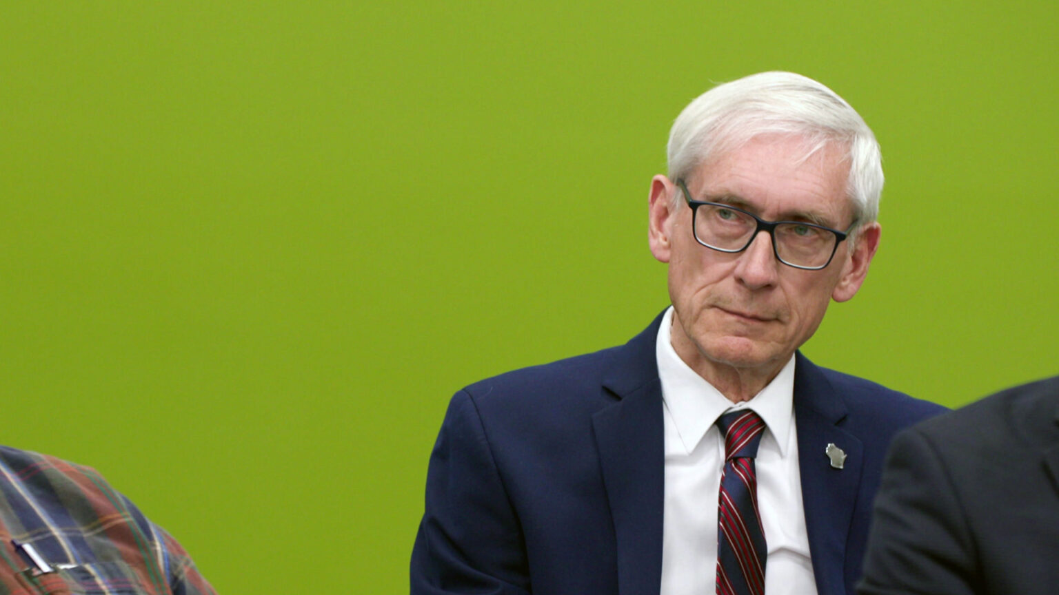 Tony Evers sits and listens, with two other people sitting in front of him.