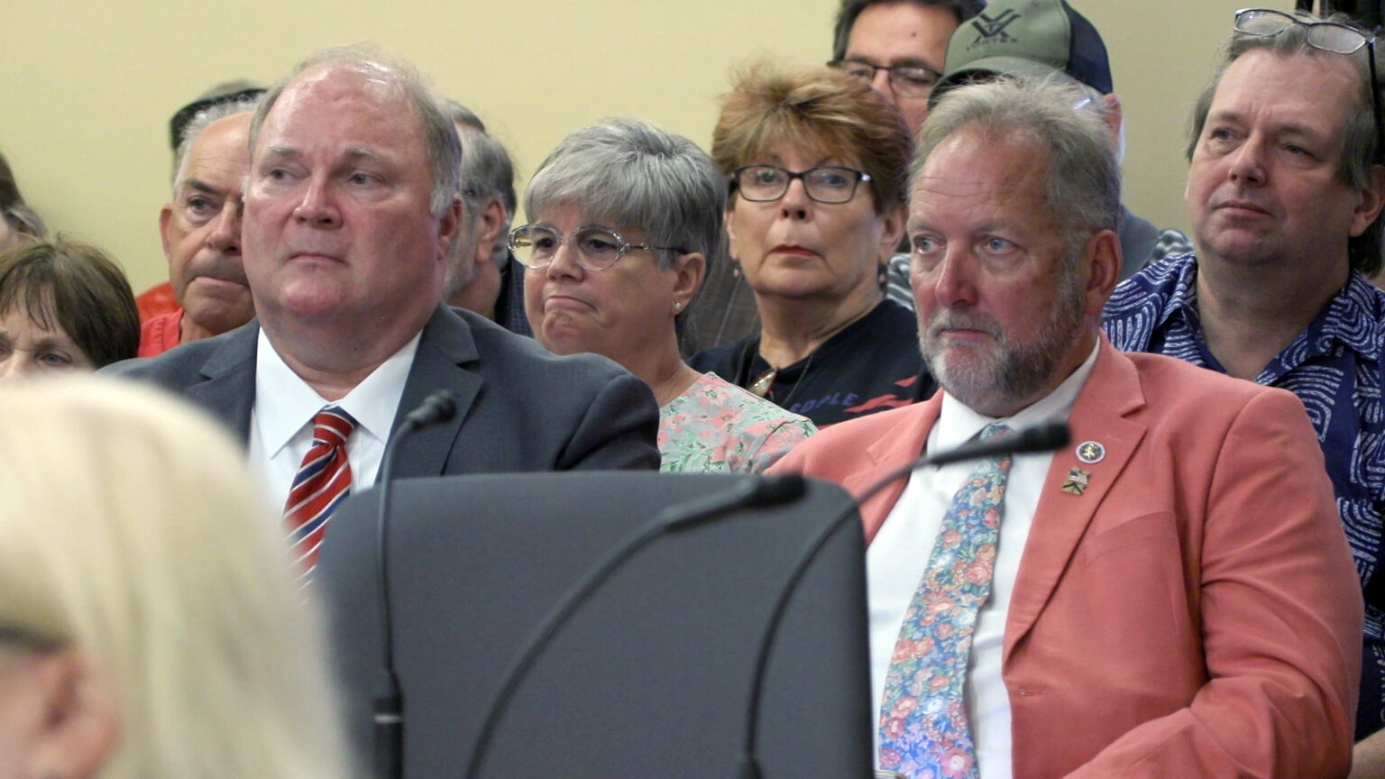 Michael Gableman and Tim Ramthun sit in a room with other people seated behind them, with an out-of-focus head of another person in the foreground.