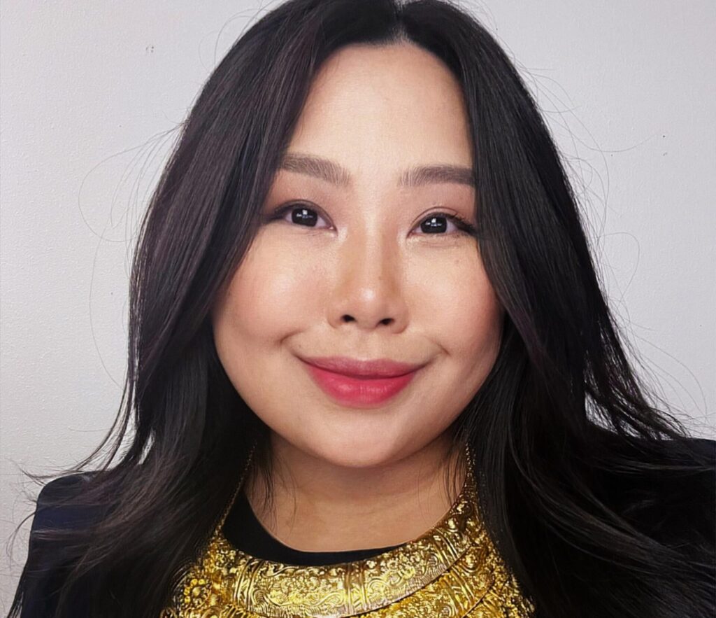 A woman wearing black with gold jewelry smiles at the camera.