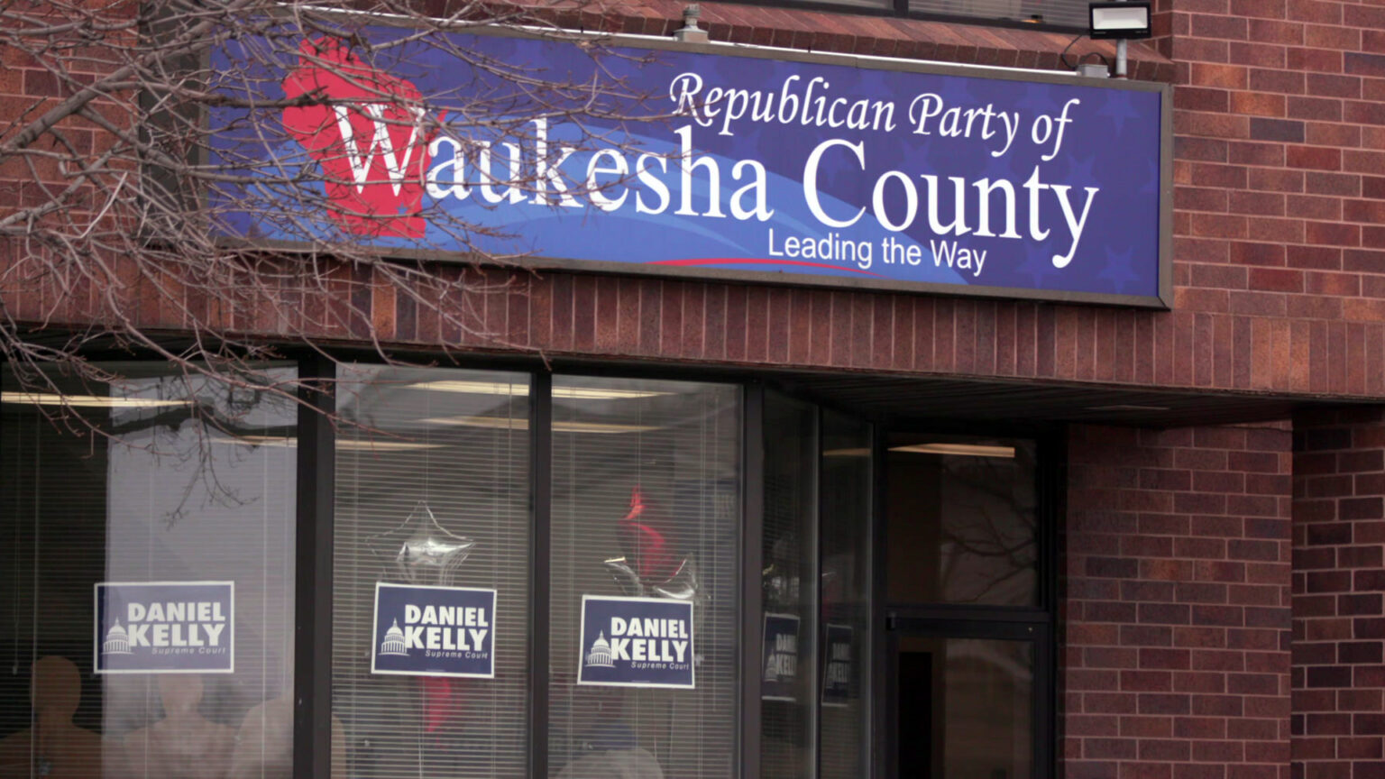 A sign reading Republican Party of Waukesha County and Leading the Way is mounted above a door into a brick building, with signs reading Daniel Kelly and Supreme Court in its windows.