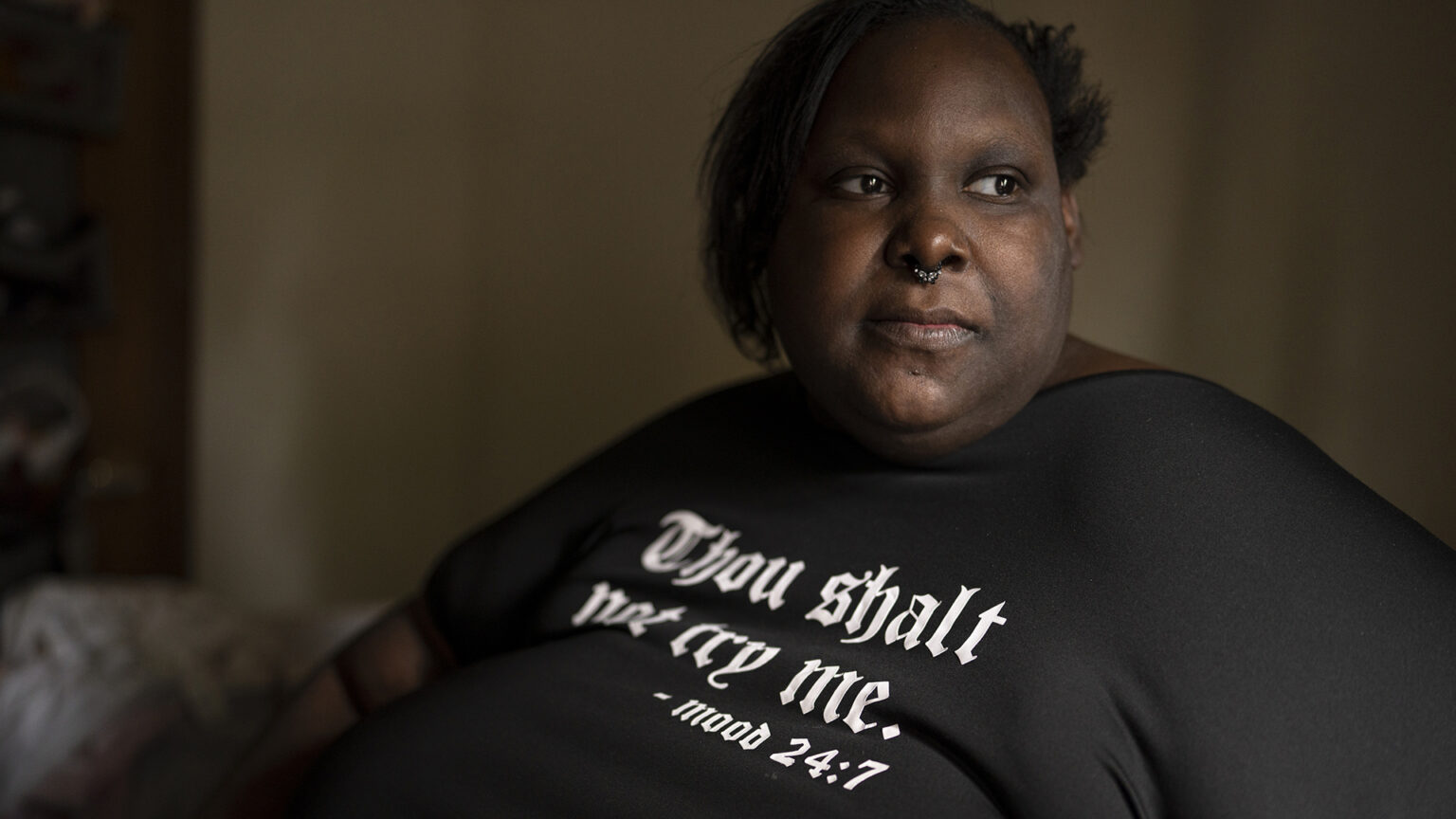 Deanna Branch looks to the side while posing for a portrait while sitting in a dark room.