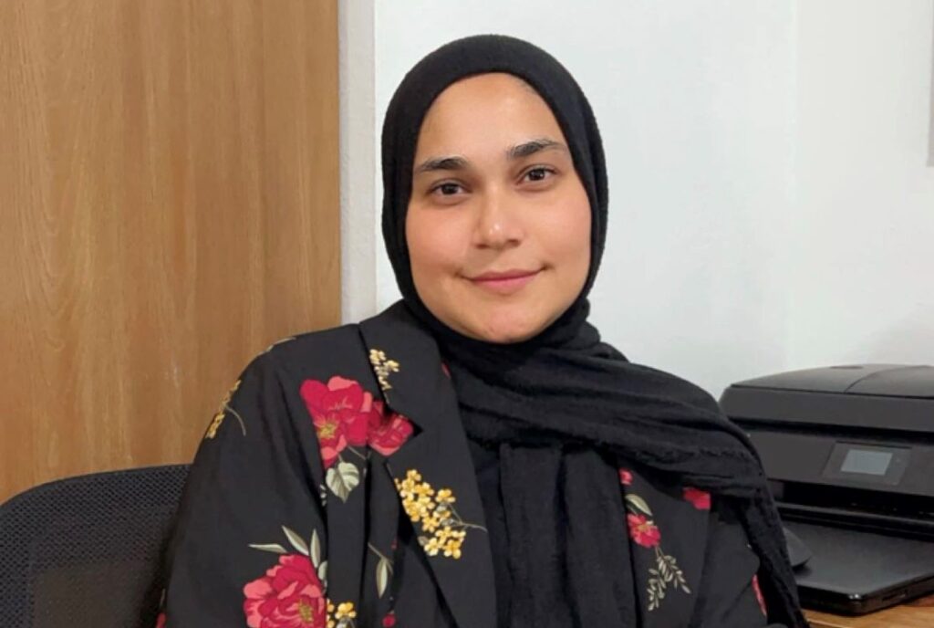 A woman in a hijab smiles at the camera.