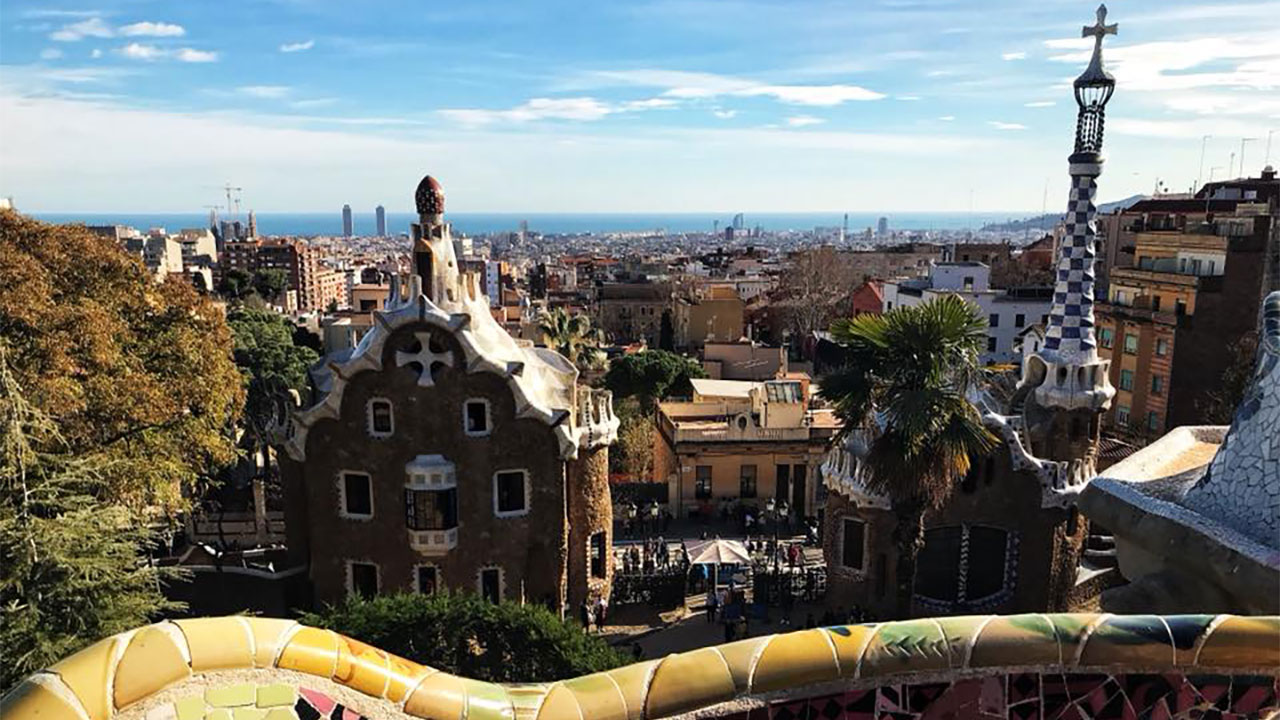 Panoramic view of Barcelona from Park Güell, showcasing Gaudí's architectural designs in the foreground, with the city skyline stretching out to the sea in the background.