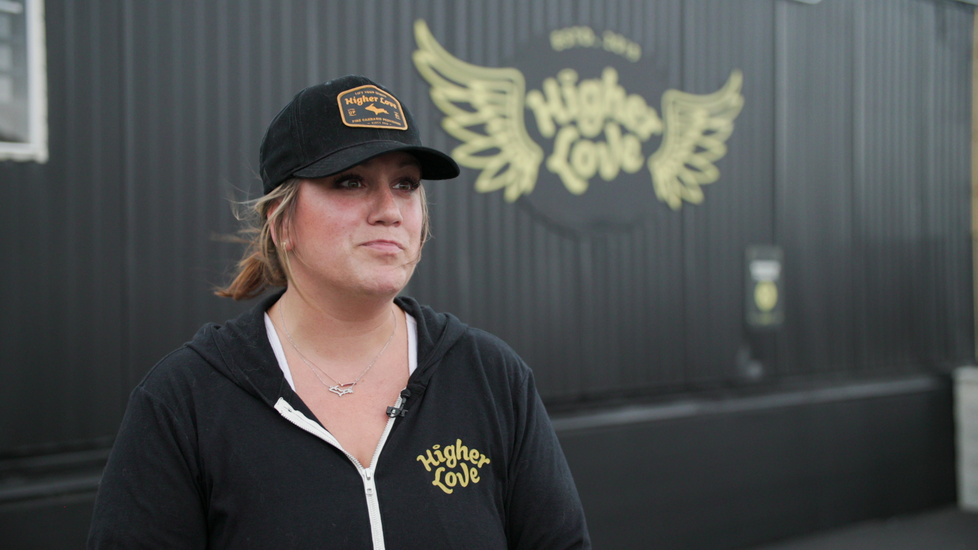 Lindsay Martwick stands outside in front of an out-of-focus shipping container with a winged logo for Higher Love.