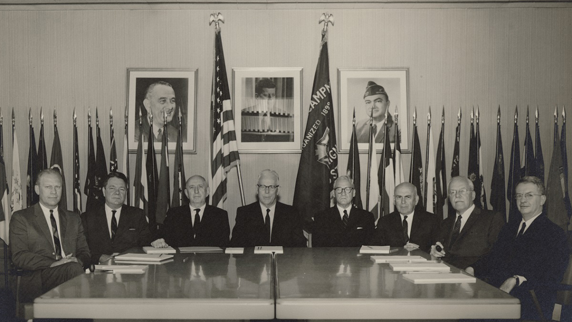 A group of men wearing suits sit at a table looking at the camera. 