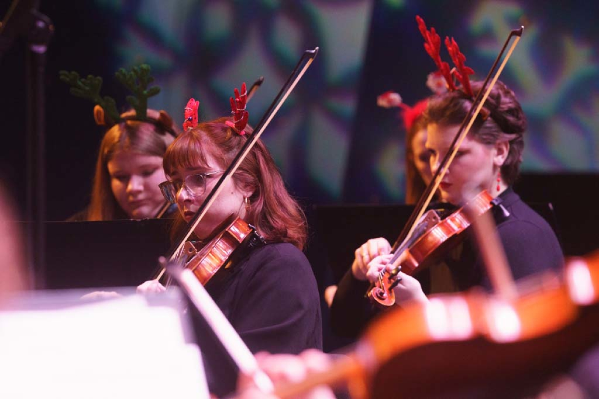 Three violinists wearing felt reindeer ears and wearing black outfits play their violins.