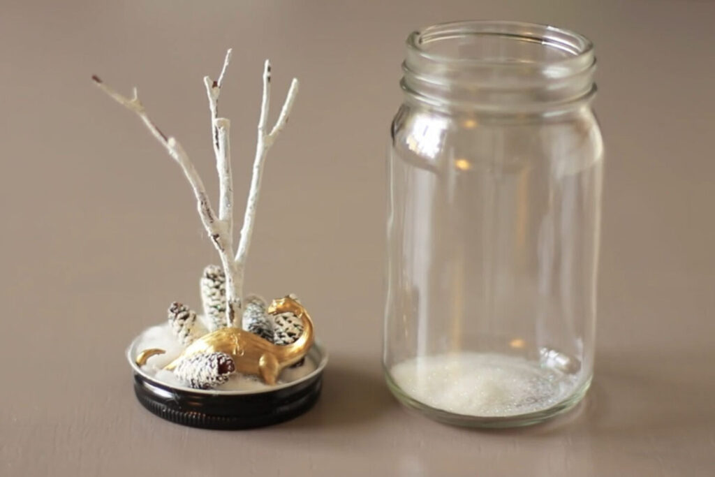 A small terrarium containing a winter scene waits for its glass jar top to be placed.