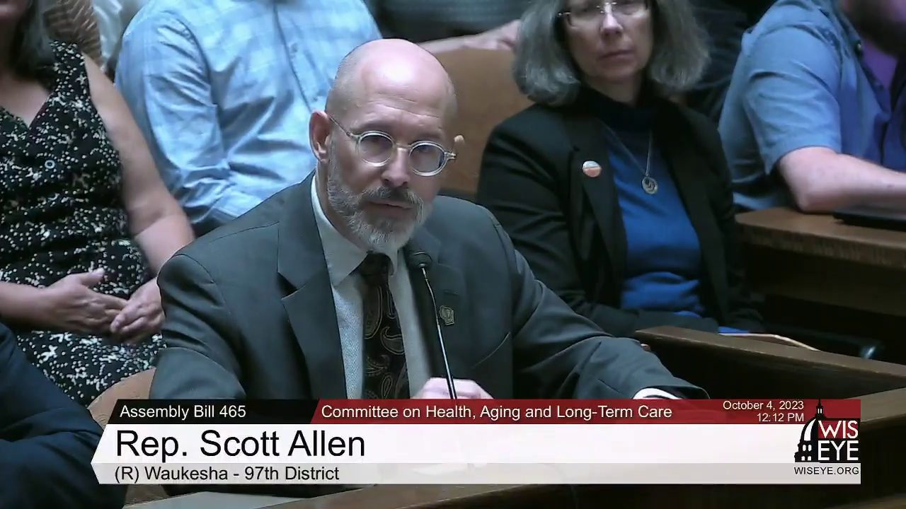A video still image shows Scott Allen sitting at a table and speaking into a microphone in a room with more people seated in the background, with a video graphic at bottom including the text "Rep. Scott Allen" and "(R) Waukesha - 97th District."