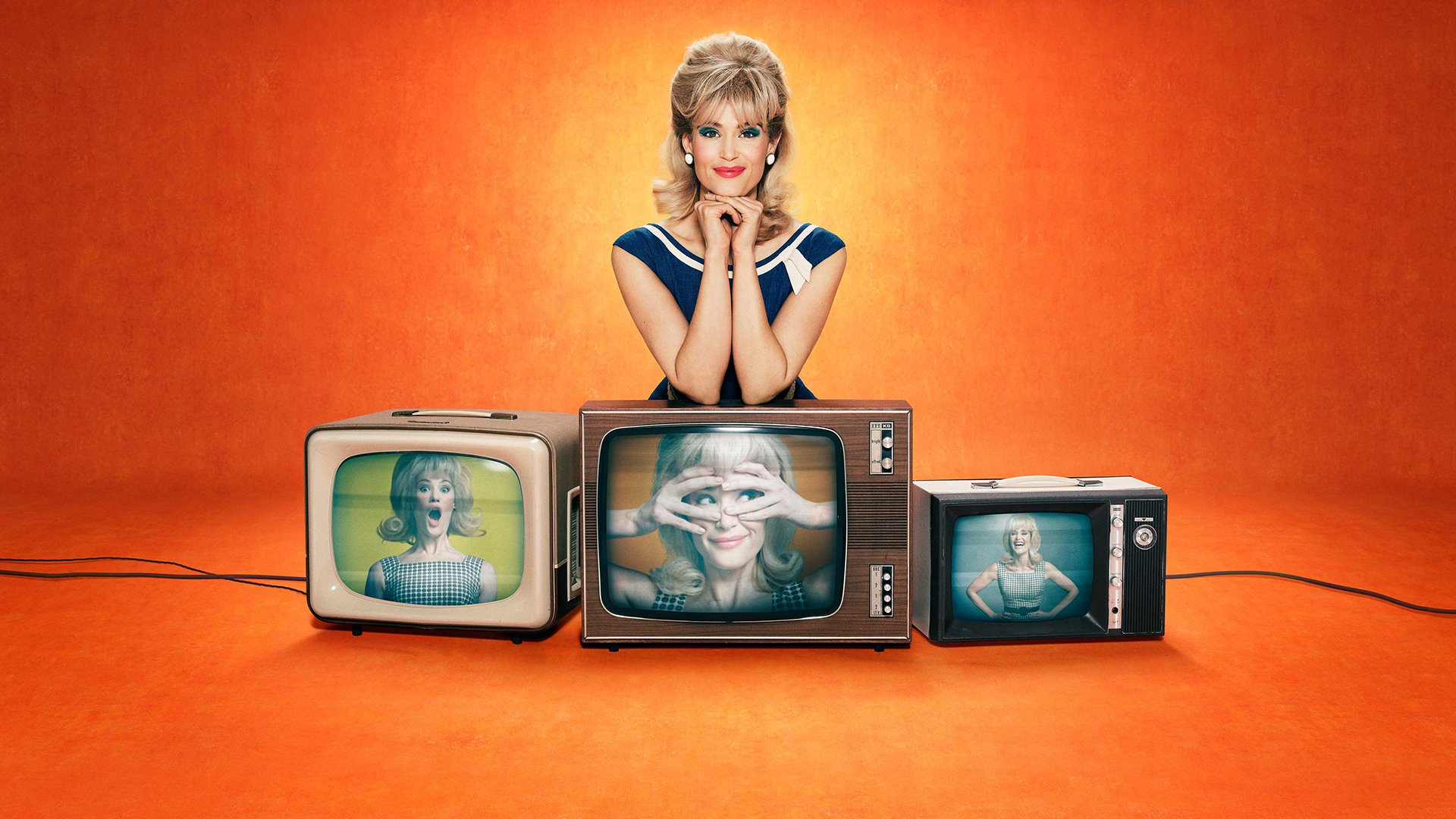 A blonde woman wearing red lipstick rests her chin on her hands while her elbows rest on top of a television screen featuring a still image of her face.