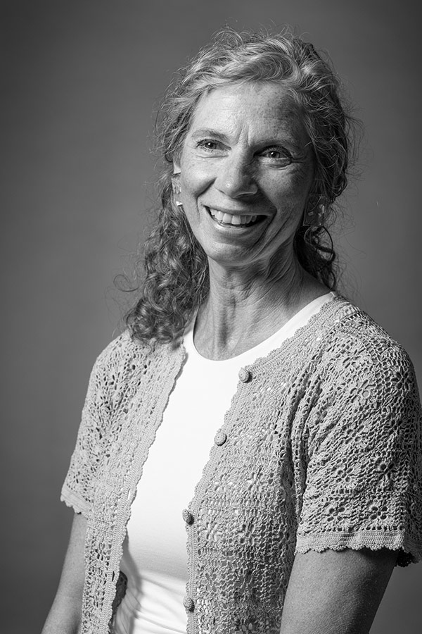 Black and white image of a smiling woman with curly hair wearing a crochet cardigan over a white top.