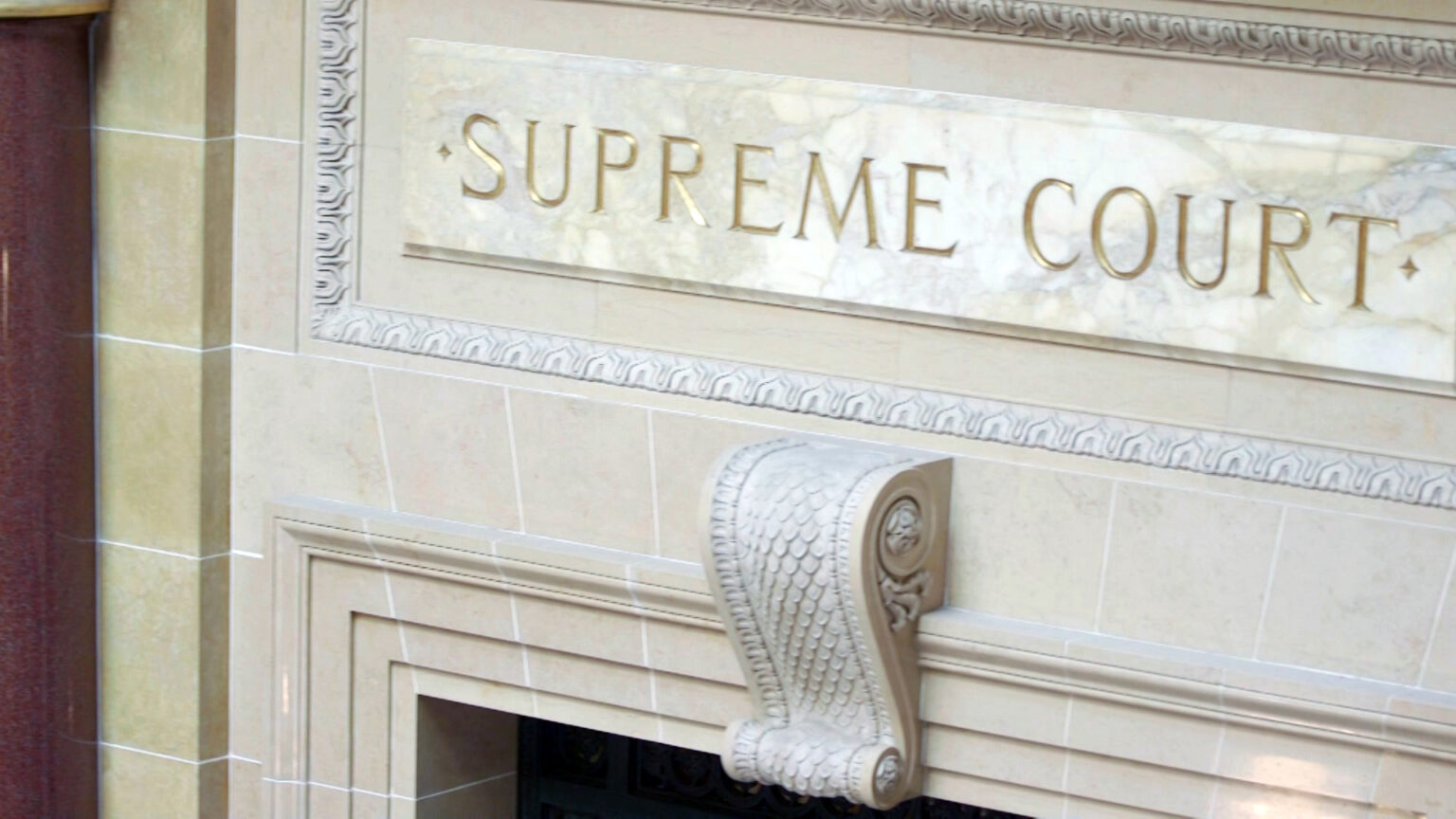 The words Supreme Court are engraved in a marble sign set into masonry above a door pediment.