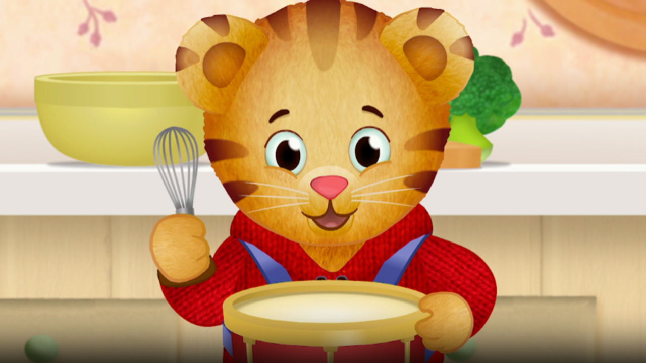 The character Daniel Tiger faces us with a cooking whisk in his hand over a mixing bowl