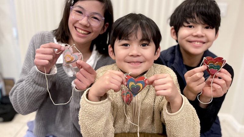 Three children are each holding a handmade heart necklace.