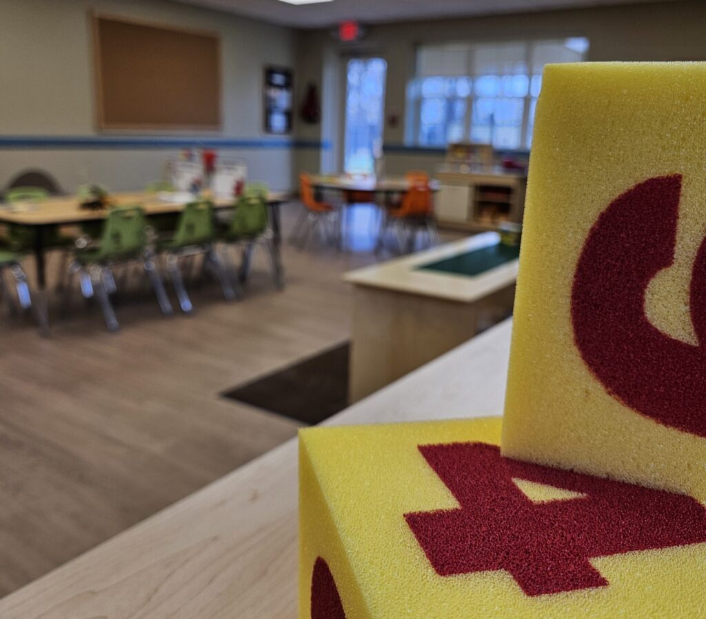 A photo of an early learning space with foam blocks in the foreground and tables and chairs in the background.
