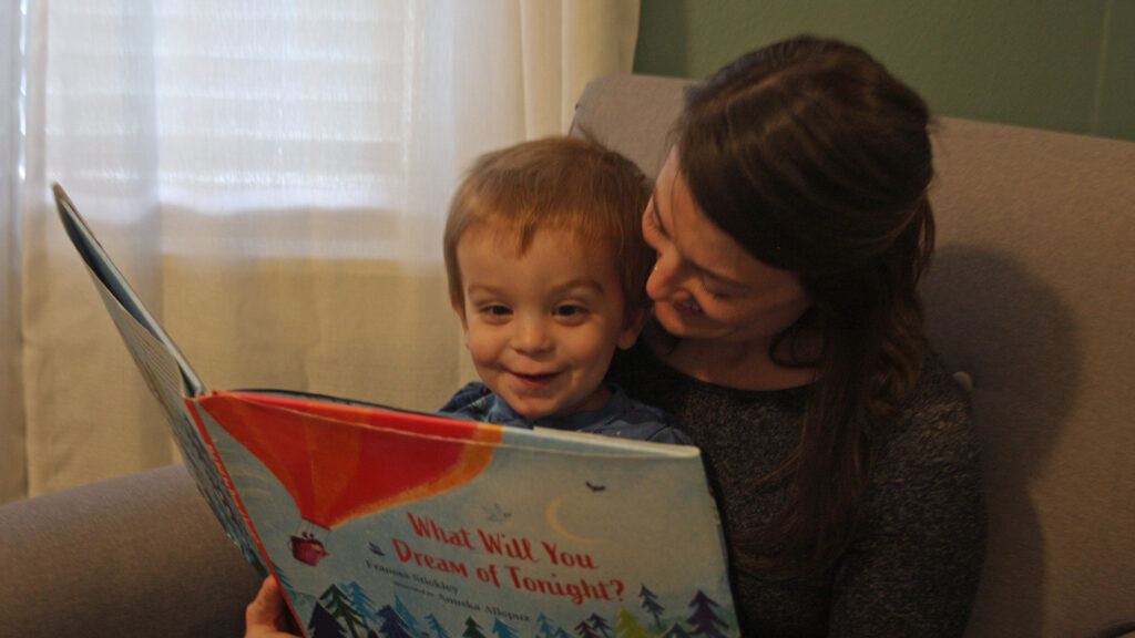 A smiling mother reads to her two-year-old son in his nursery.