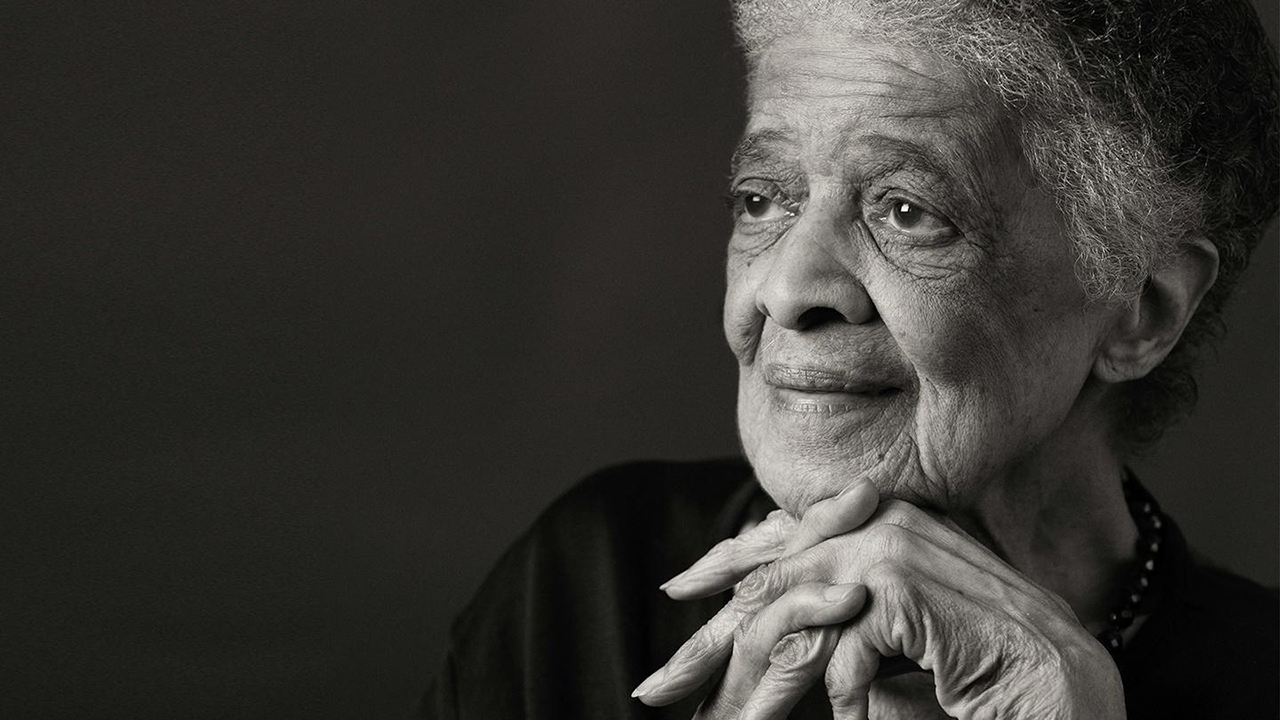 Black and white photo of an elderly woman with a thoughtful expression, resting chin on hands.