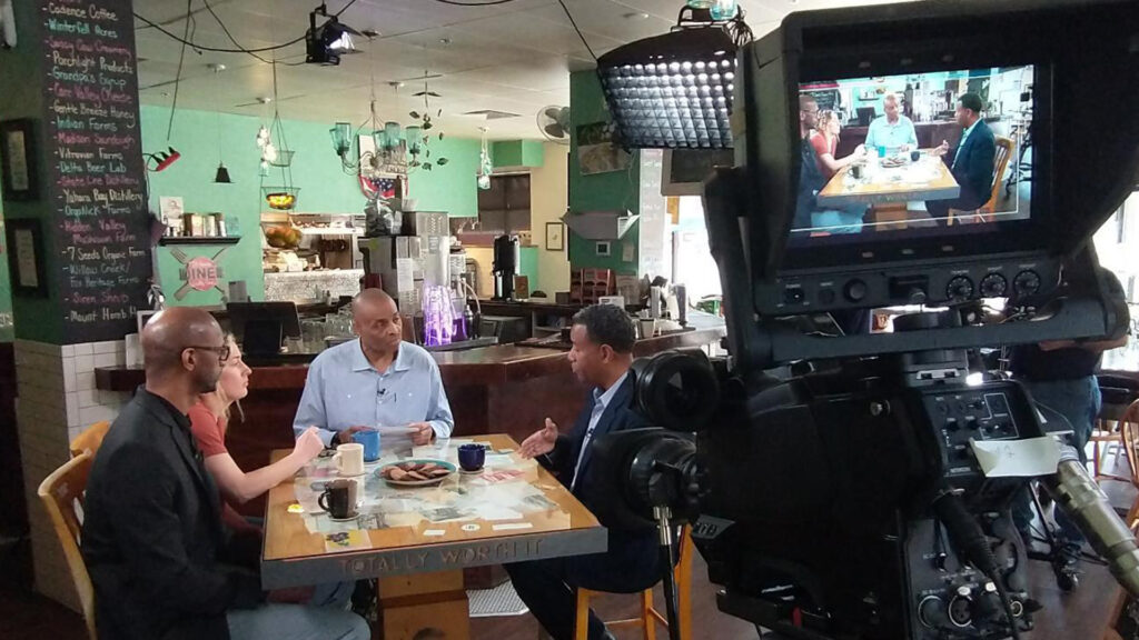 Three people having a conversation at a table in a cafe during a video production shoot.