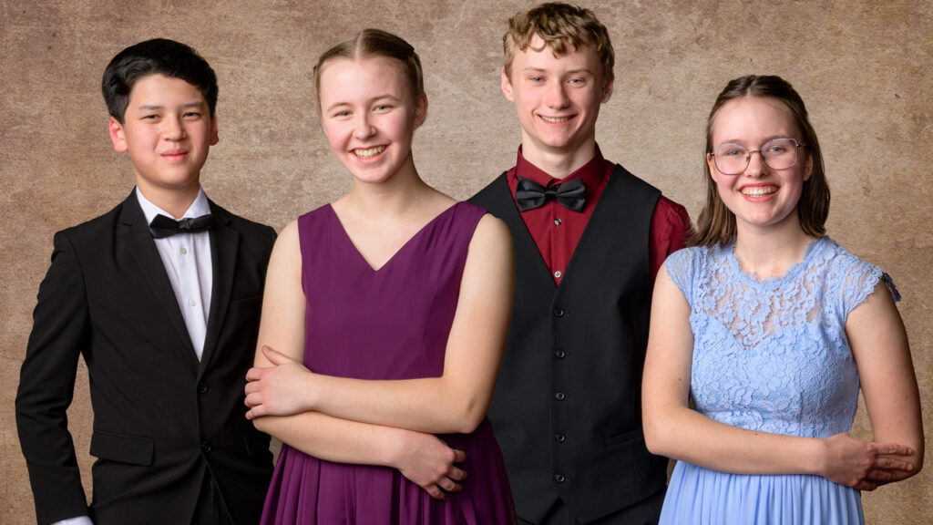 Four high school students in formal attire in a portrait studio stand together and smile.