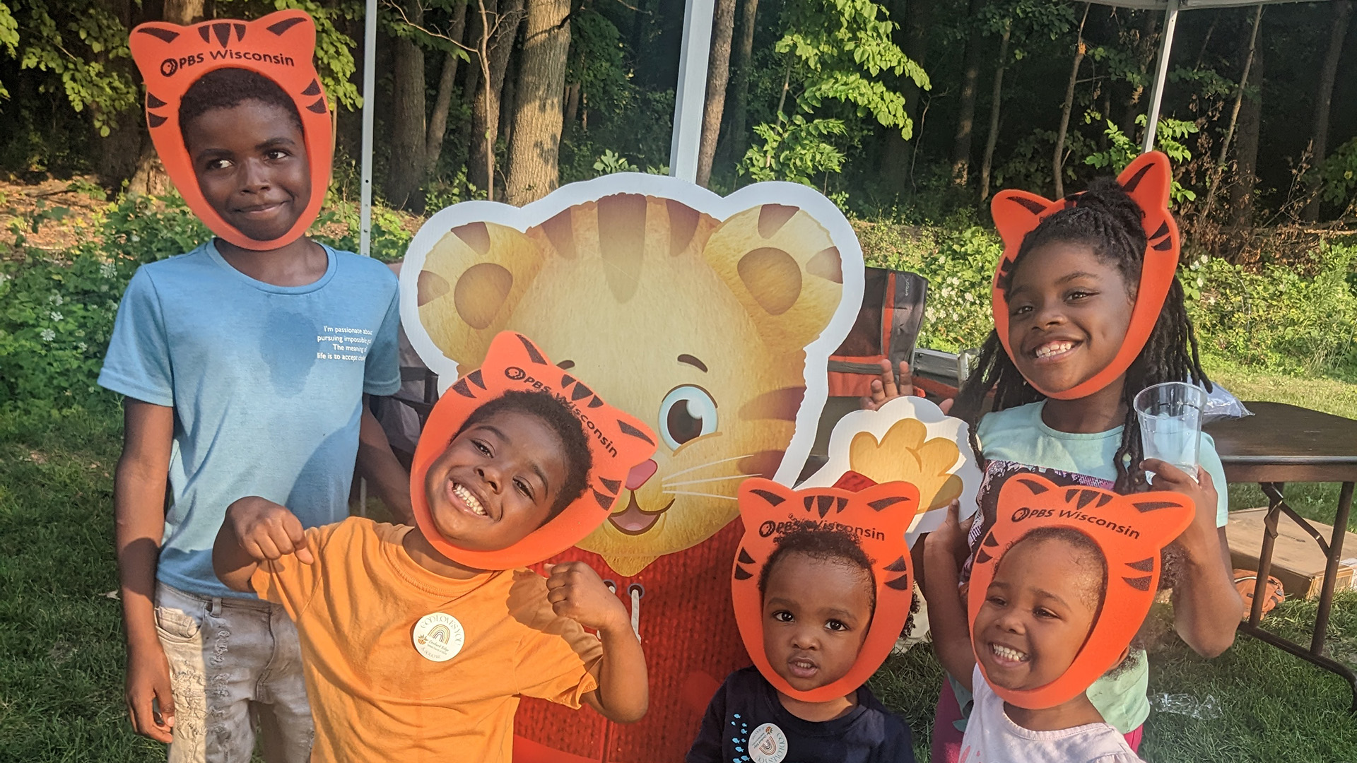 A group of children dressed like Daniel Tiger around a Daniel Tiger sign.