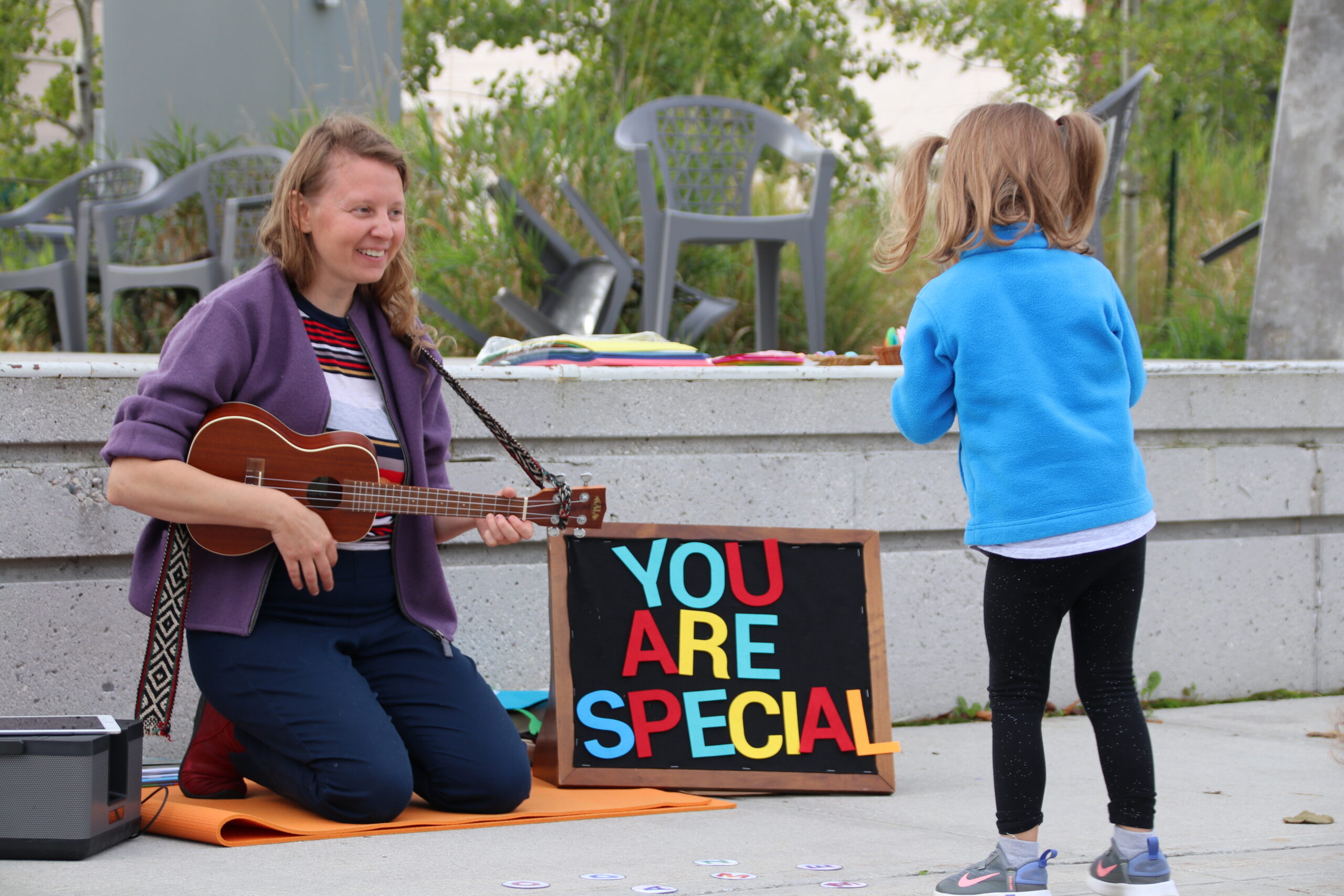 Image of woman playing a guitar while a small girl dances in front of a sign that says You Are Special