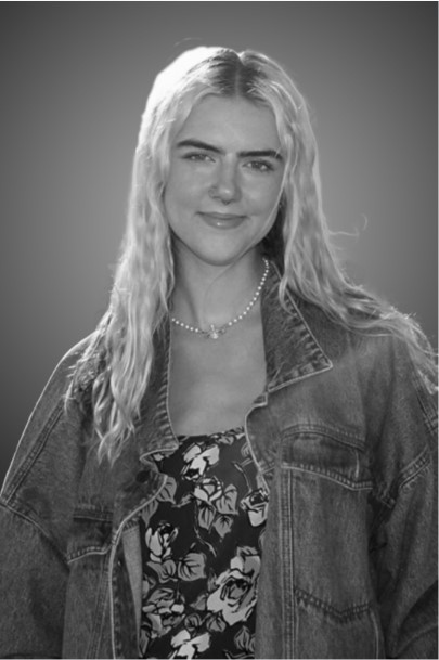Black and white portrait of a woman with long hair, denim jacket, and a floral top, wearing a necklace.