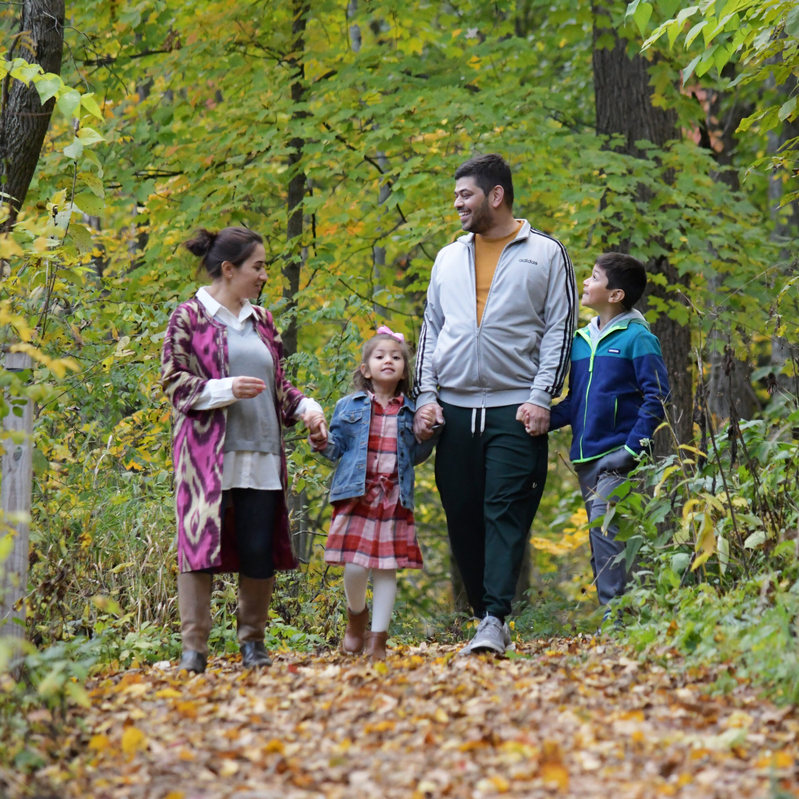 Family of four enjoying a walk in a forest with autumn leaves on the ground.