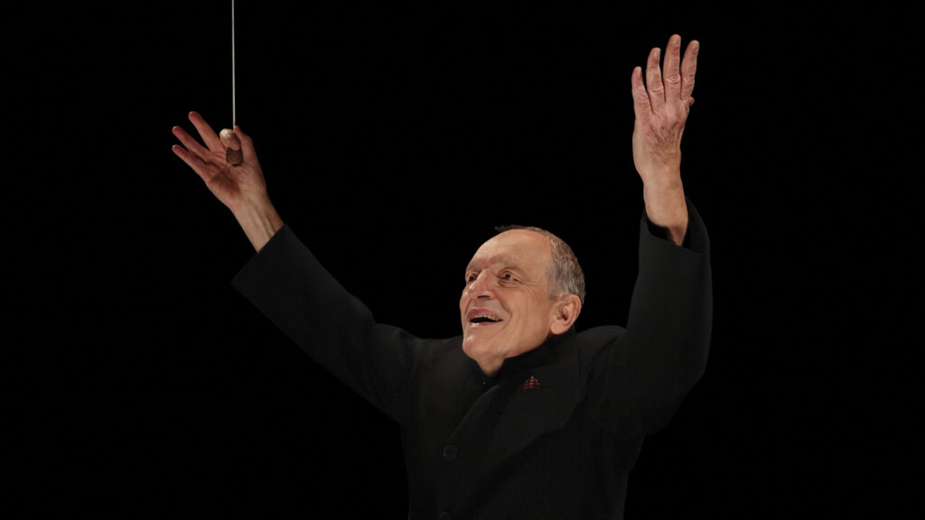 Conductor John DeMain smiles as he waves his baton.