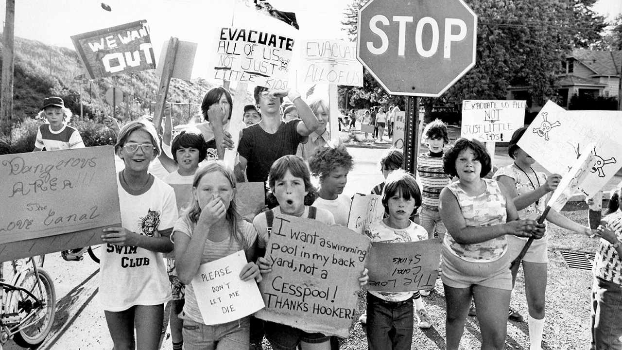 A crowd of children and young adults hold signs up featuring various sayings while marching in the street.