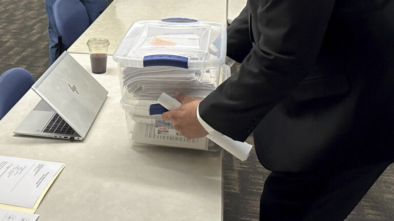 Matthew Snorek sets a plastic storage box with clasps on its lid and filled with a papers on the surface of a table that also has a laptop computer, plastic beverage container and other papers on its surface.