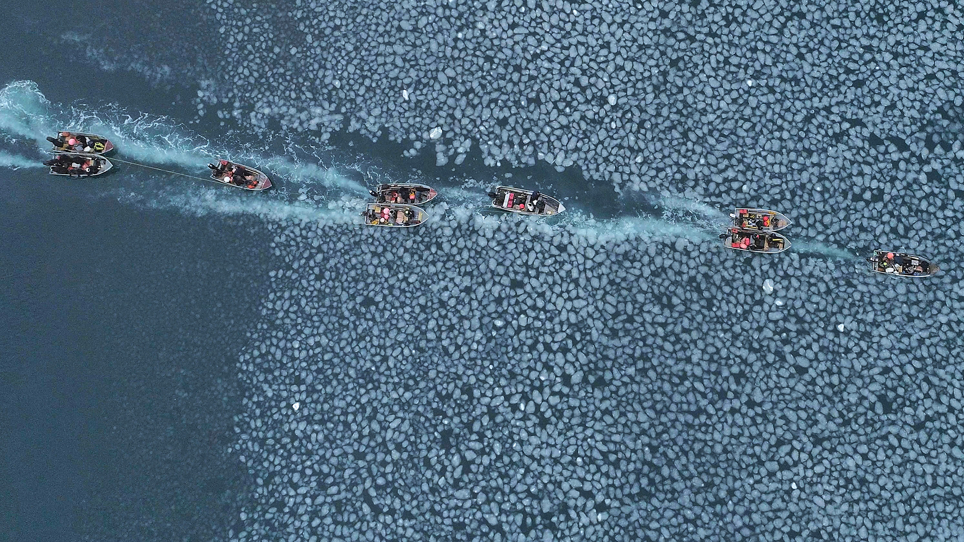 Birds-eye view of boats driving through ice on the Pacific Ocean.