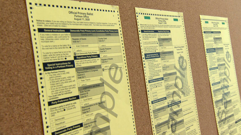Three sample ballots showing candidates in party primaries are stapled to a cork board.