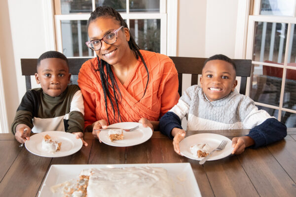 A mom and two children sit at a table with a carrot cake they made.