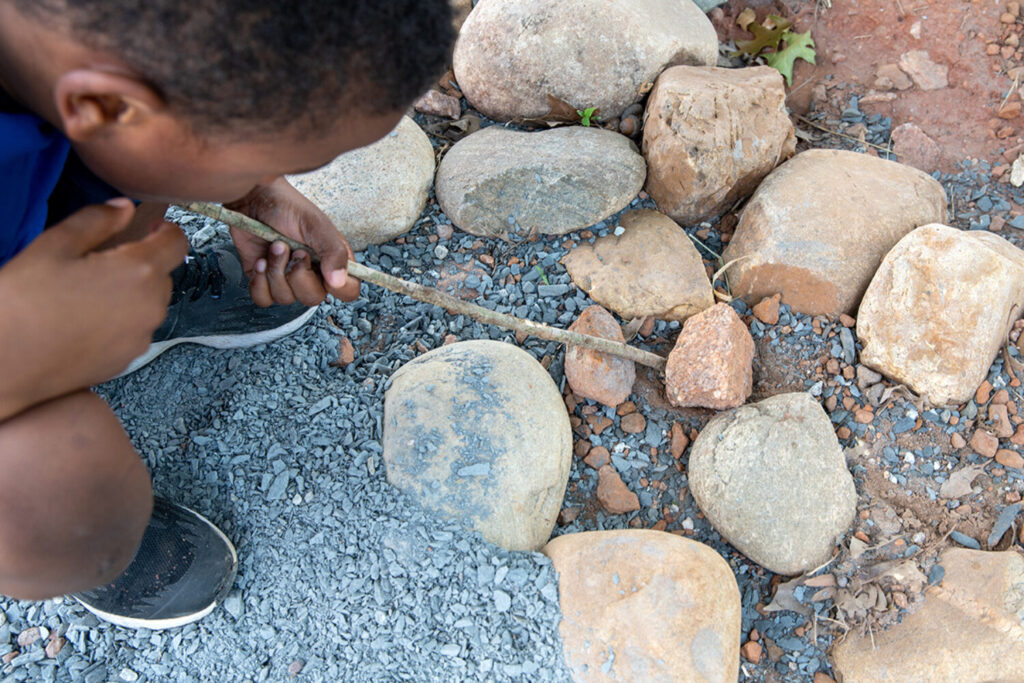 A young child crouches near a pile of rocks.