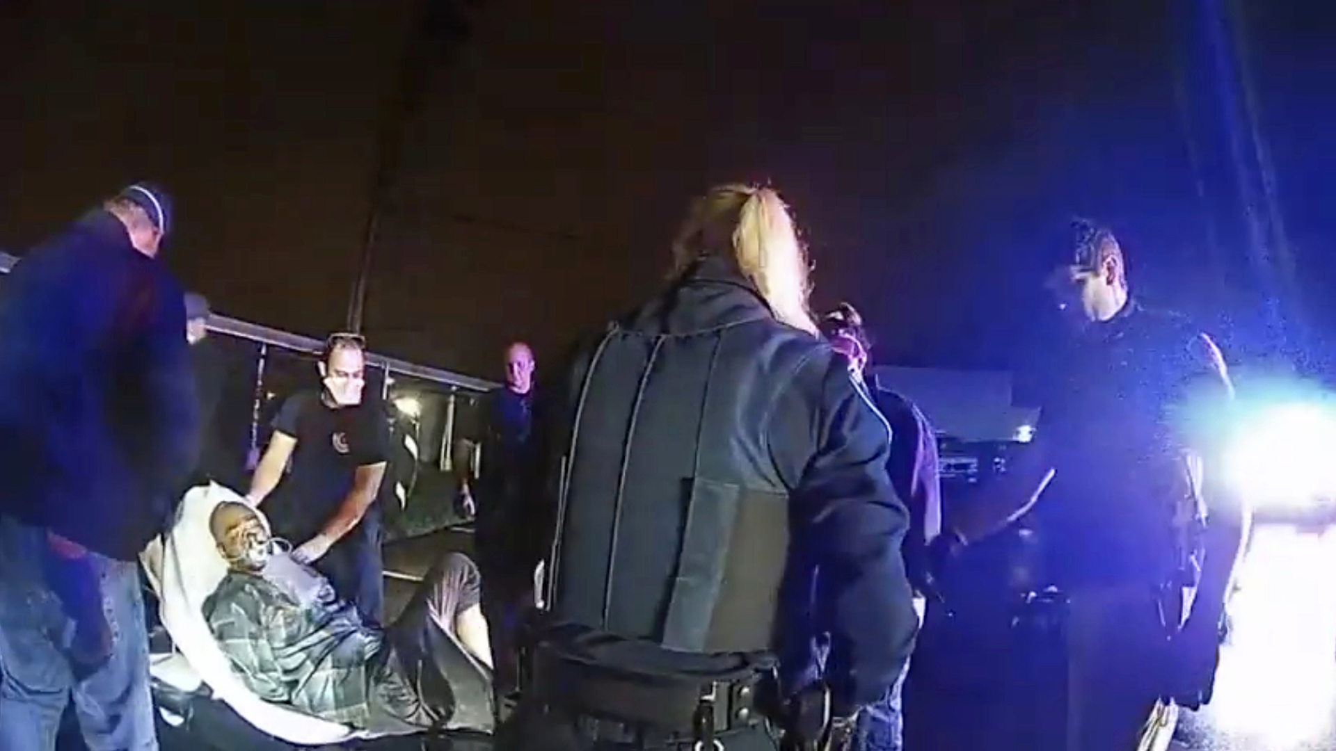 Demetrio Jackson lays unconscious on a gurney while wearing a bag valve mask, with multiple police officers standing around him under a night sky.