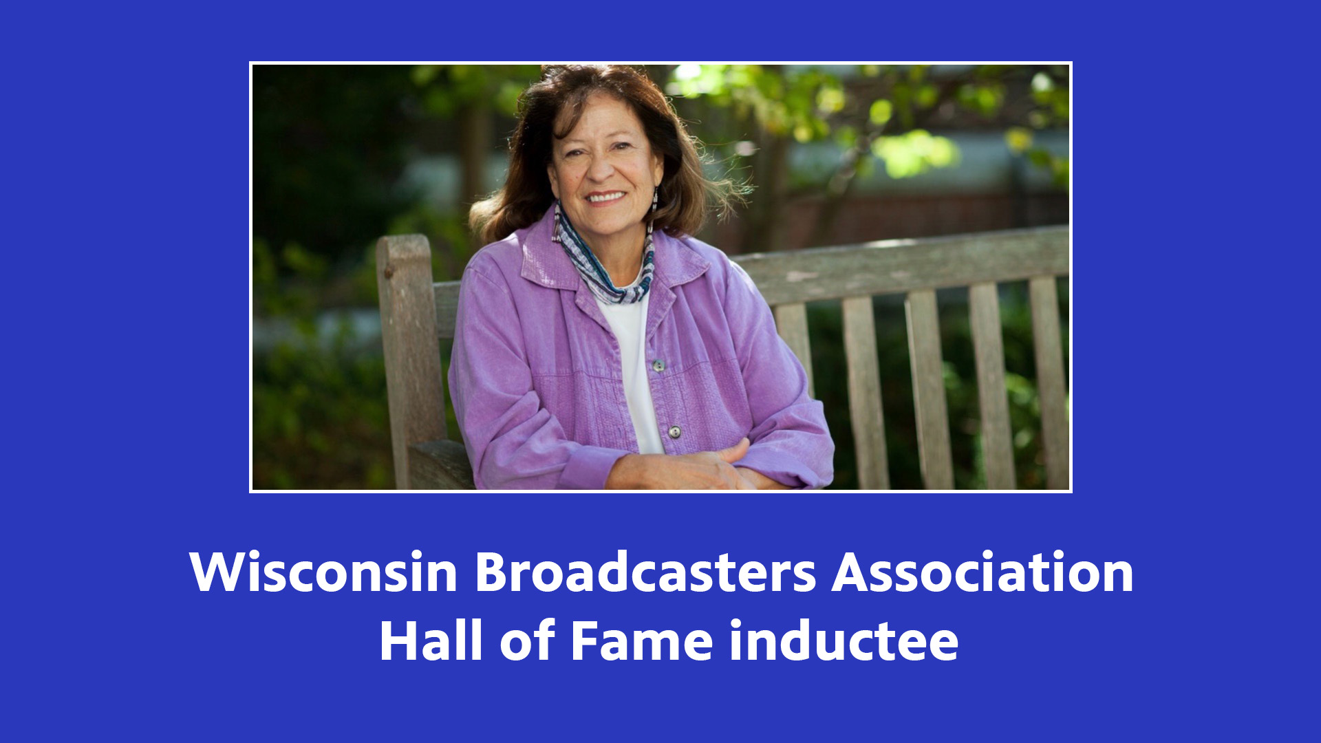 Wisconsin Broadcasters Association Hall of Fame inductee Patty Loew, a former PBS Wisconsin host and producer, sitting on a park bench with a blue background.