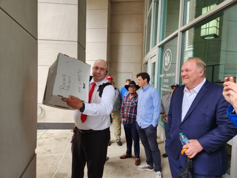 Petitioners to recall Robin Vos stand outside the Dane County Courthouse with a box labeled Racine recall