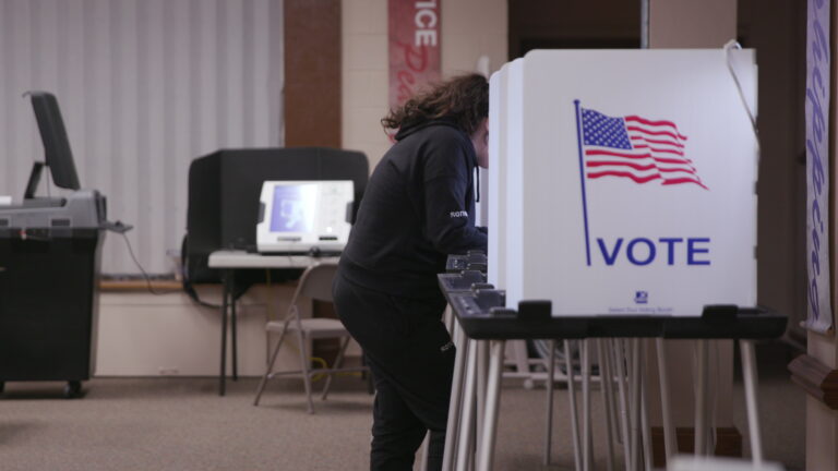 A voter hunches over their ballot in a voting booth.