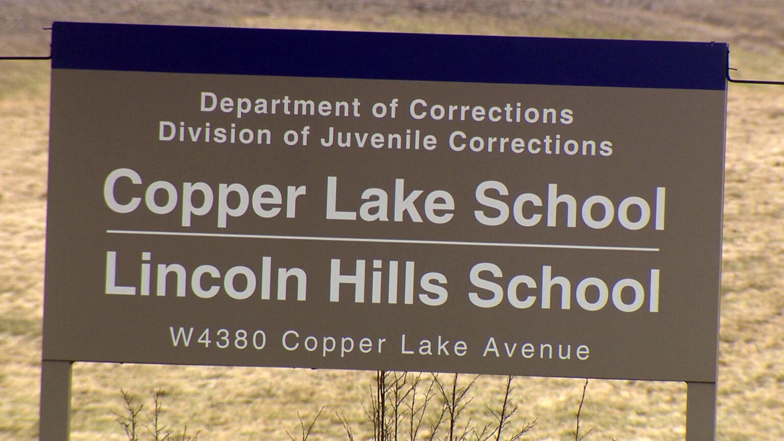 An entrance sign with the words Department of Corrections, Division of Juvenile Corrections, Copper Lake School, Lincoln Hills School and the address W 4380 Copper Lake Avenue stands in front of a field.