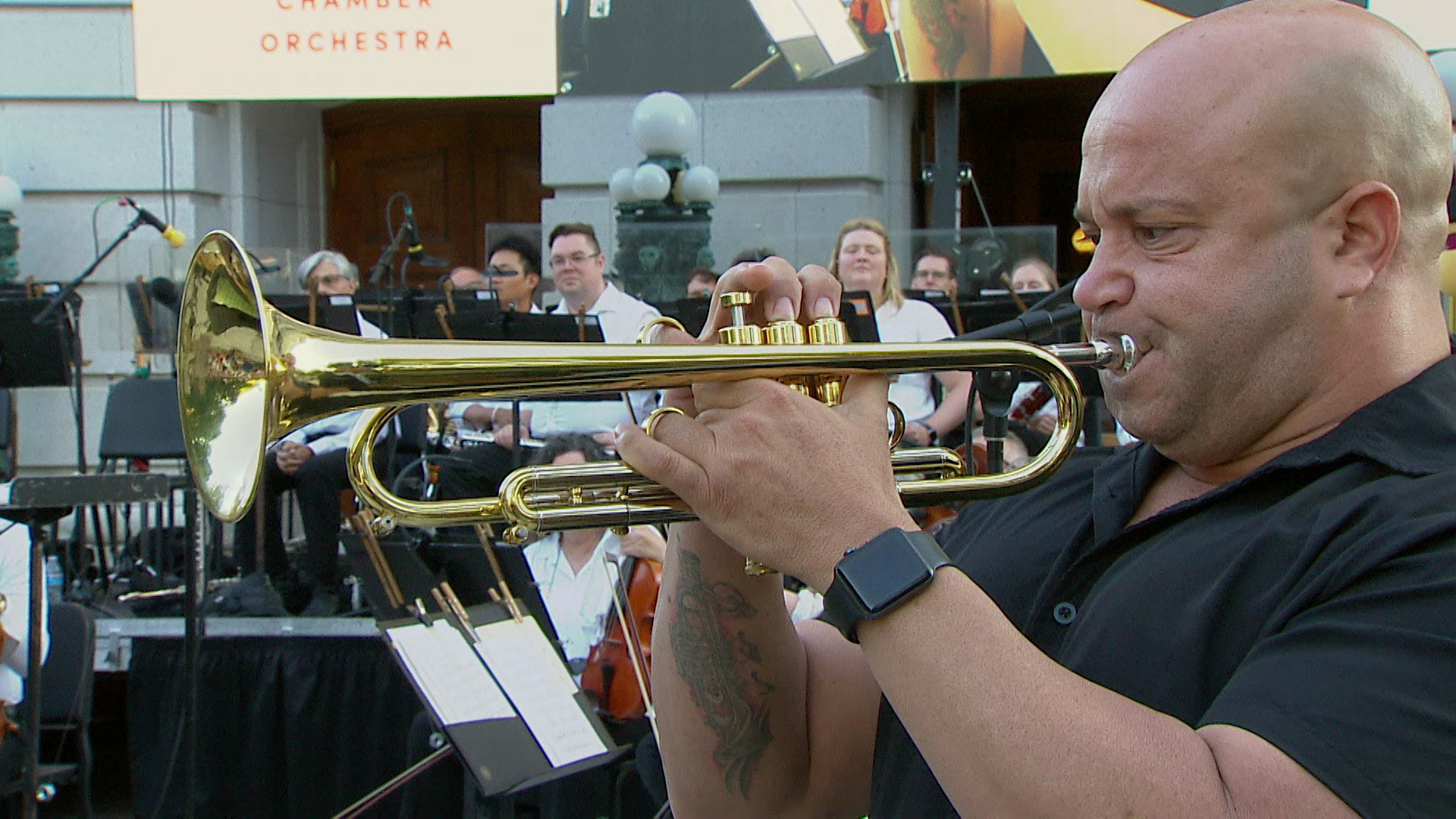 A bald man plays the trumpet