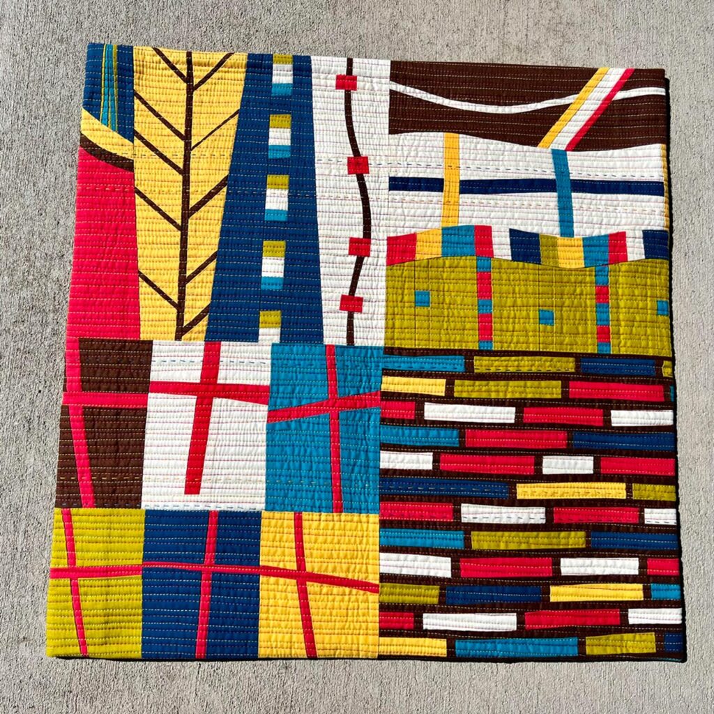 A small, square quilt with bright, modern colors and geometric patterns.