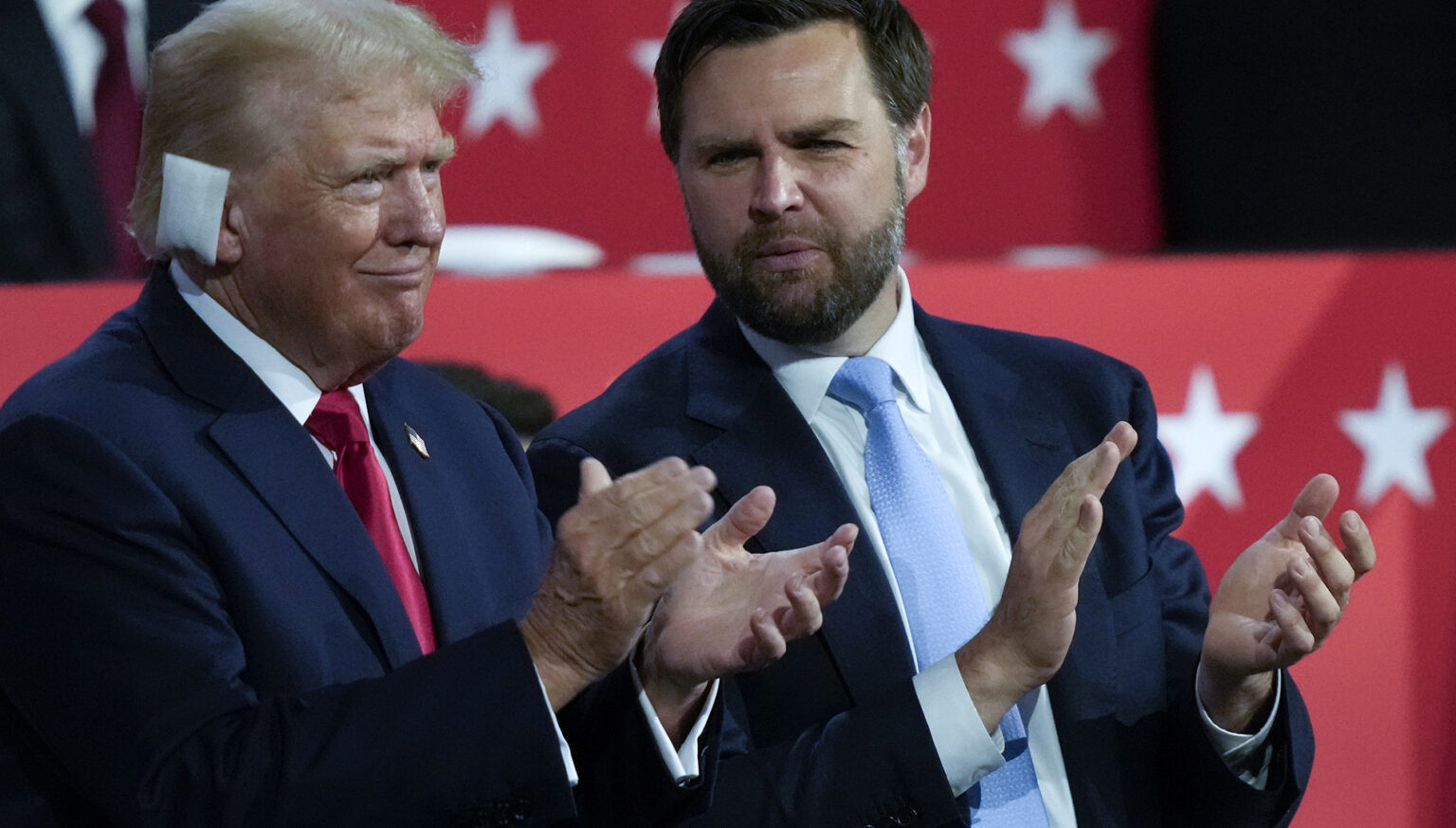 Donald Trump, who has a bandage over his right ear, and JD Vance clap their hands while standing.