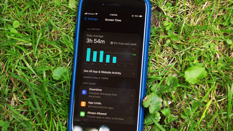 A smartphone showing a screen time app that includes a chart showing daily averages and options to limit usage sits on a lawn outside.